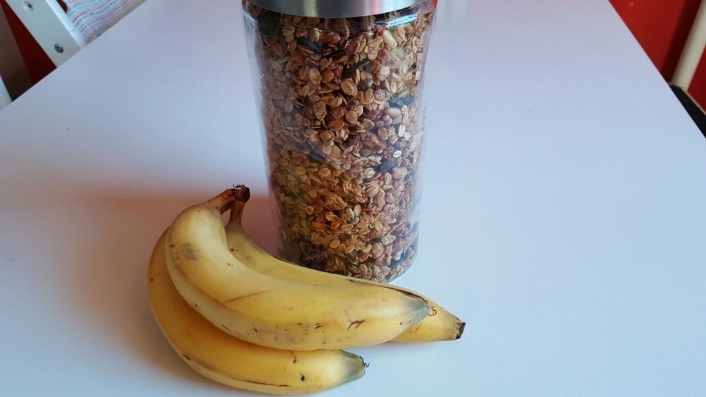 Banana Bread Müsli im Behälter mit Bananen auf weißem Untergrund